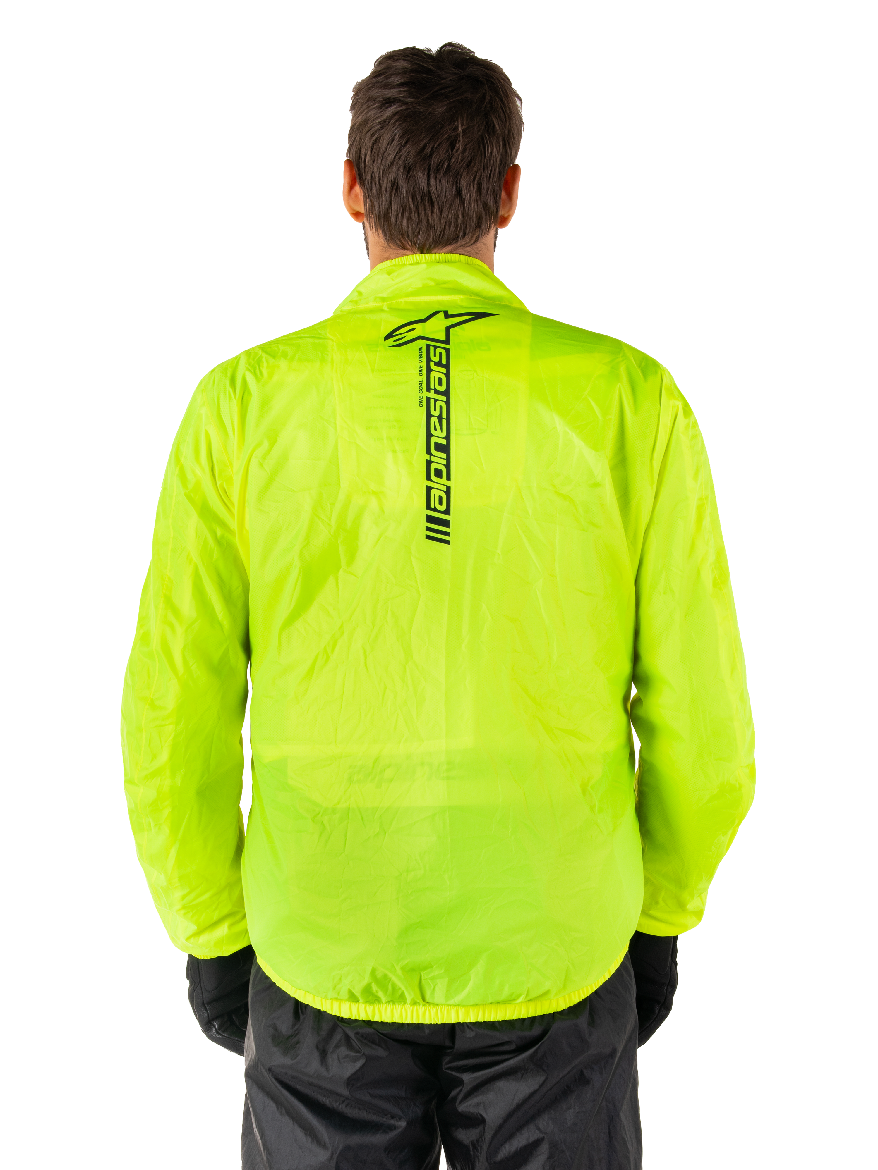 Veste Alpinestars Hurricane Rain V2, veste de pluie moto, jaune fluo, vue arrière montrant le logo Alpinestars noir vertical au centre du dos, tissu imperméable léger, portée avec un pantalon et des gants de moto noirs