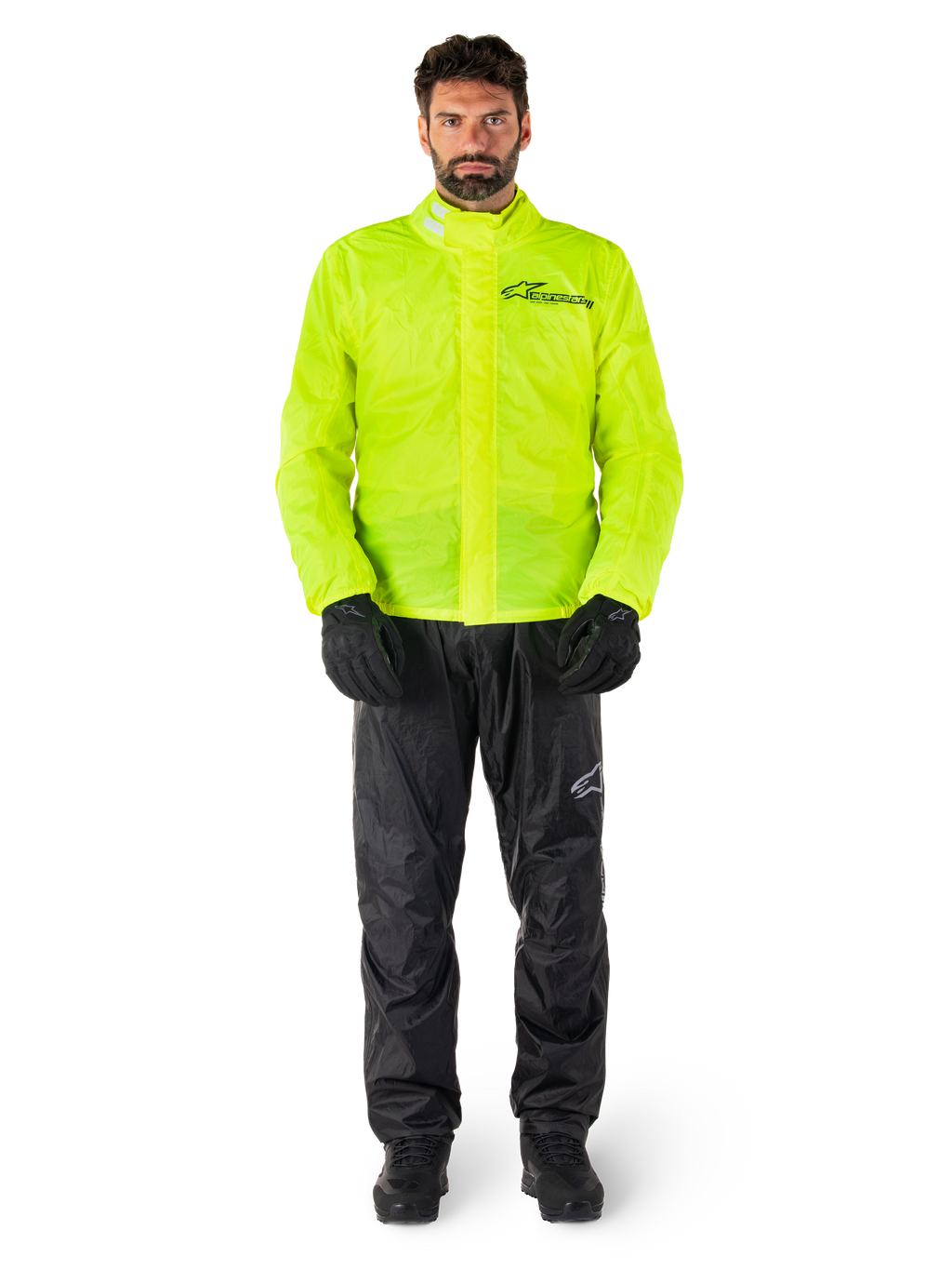 Ensemble veste et pantalon de pluie Alpinestars Hurricane Rain V2, jaune fluo et noir, combinaison de pluie moto imperméable portée avec des gants et des bottes noirs, avec le logo Alpinestars sur la poitrine et la jambe