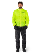 Ensemble veste et pantalon de pluie Alpinestars Hurricane Rain V2, jaune fluo et noir, combinaison de pluie moto imperméable portée avec des gants et des bottes noirs, avec le logo Alpinestars sur la poitrine et la jambe