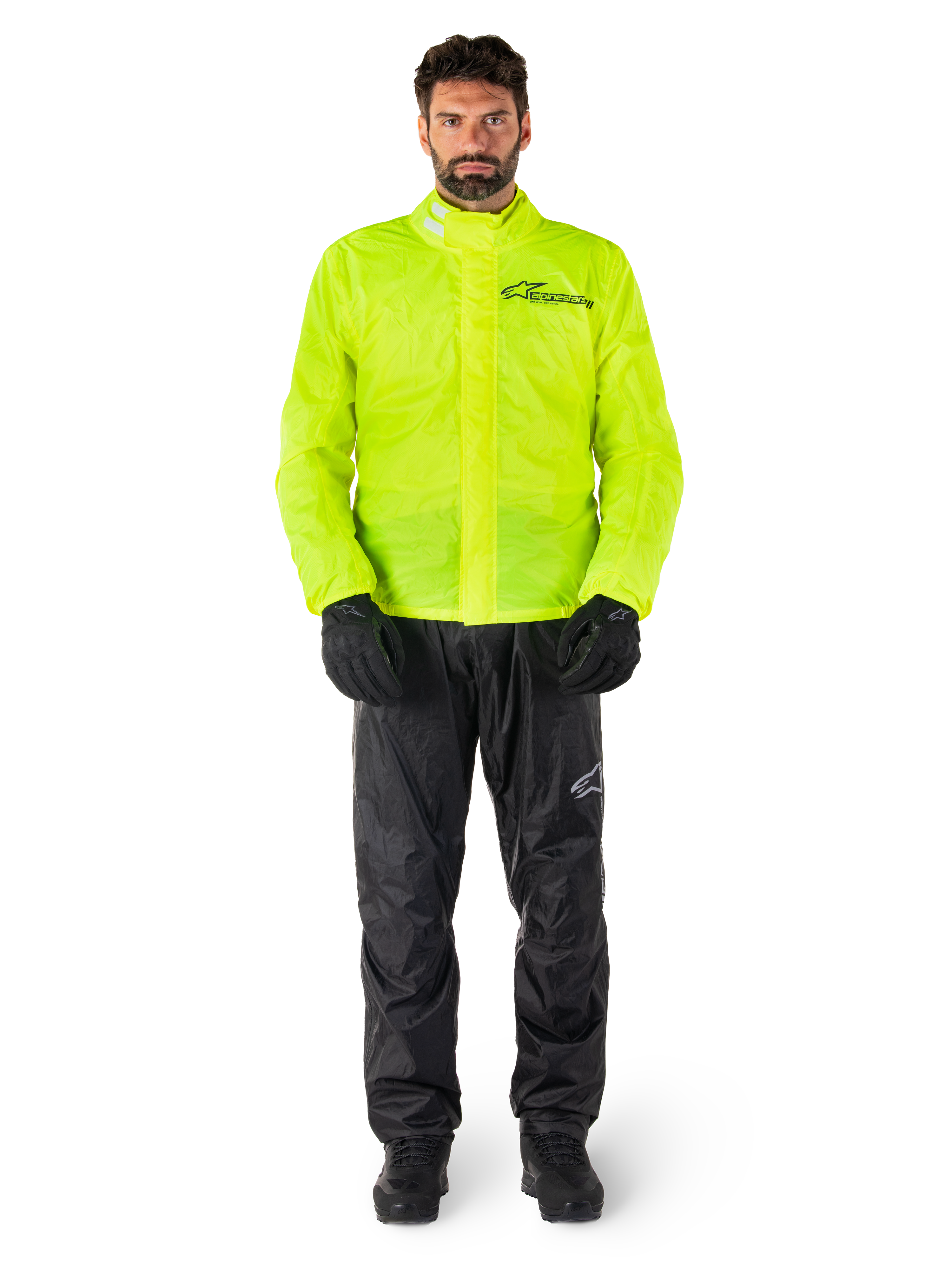 Ensemble veste et pantalon de pluie Alpinestars Hurricane Rain V2, jaune fluo et noir, combinaison de pluie moto imperméable portée avec des gants et des bottes noirs, avec le logo Alpinestars sur la poitrine et la jambe