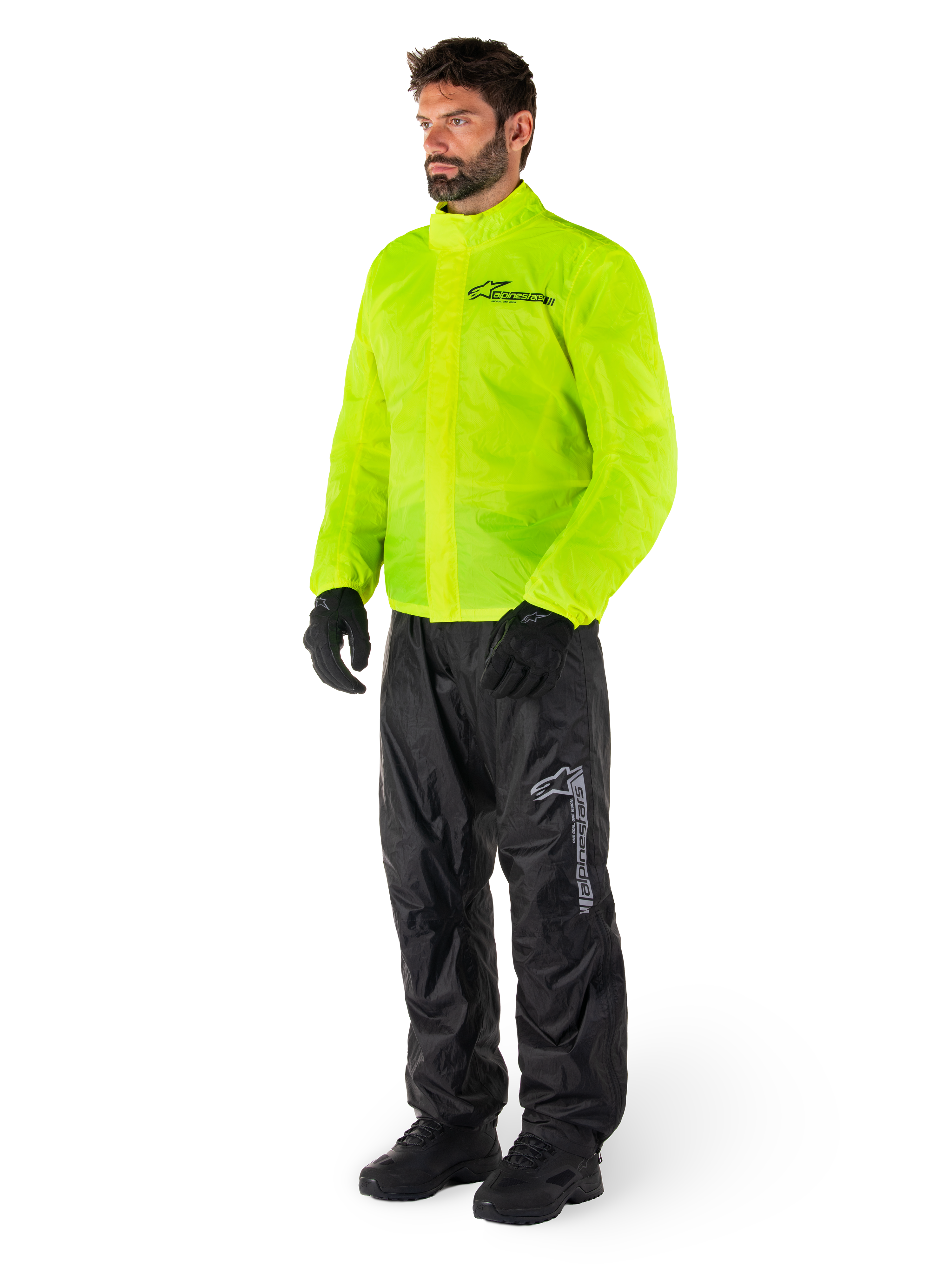 Homme portant la veste Alpinestars Hurricane Rain V2 en jaune fluo et le pantalon Hurricane Rain V2 en noir, équipement de pluie moto imperméable haute visibilité, logos réfléchissants sur la poitrine et la cuisse, tenue complète avec gants et bottes noirs