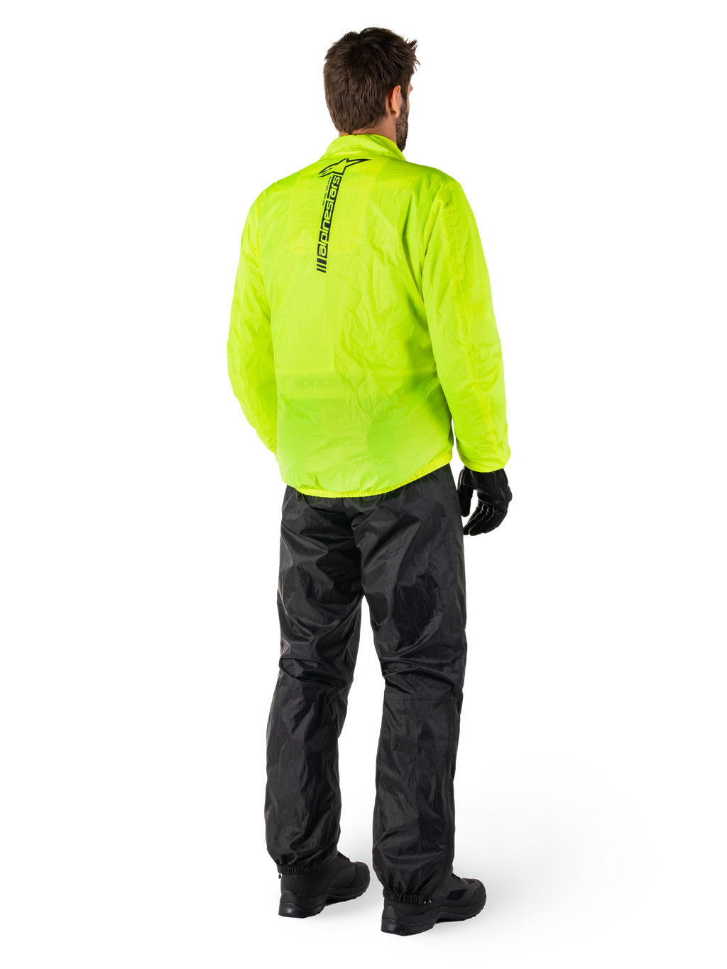 Personne vue de dos portant la veste Alpinestars Hurricane Rain V2 en Jaune Fluo et le pantalon Hurricane Rain V2 en Noir, logo vertical au dos de la veste, équipement de pluie moto imperméable avec gants et bottes noirs