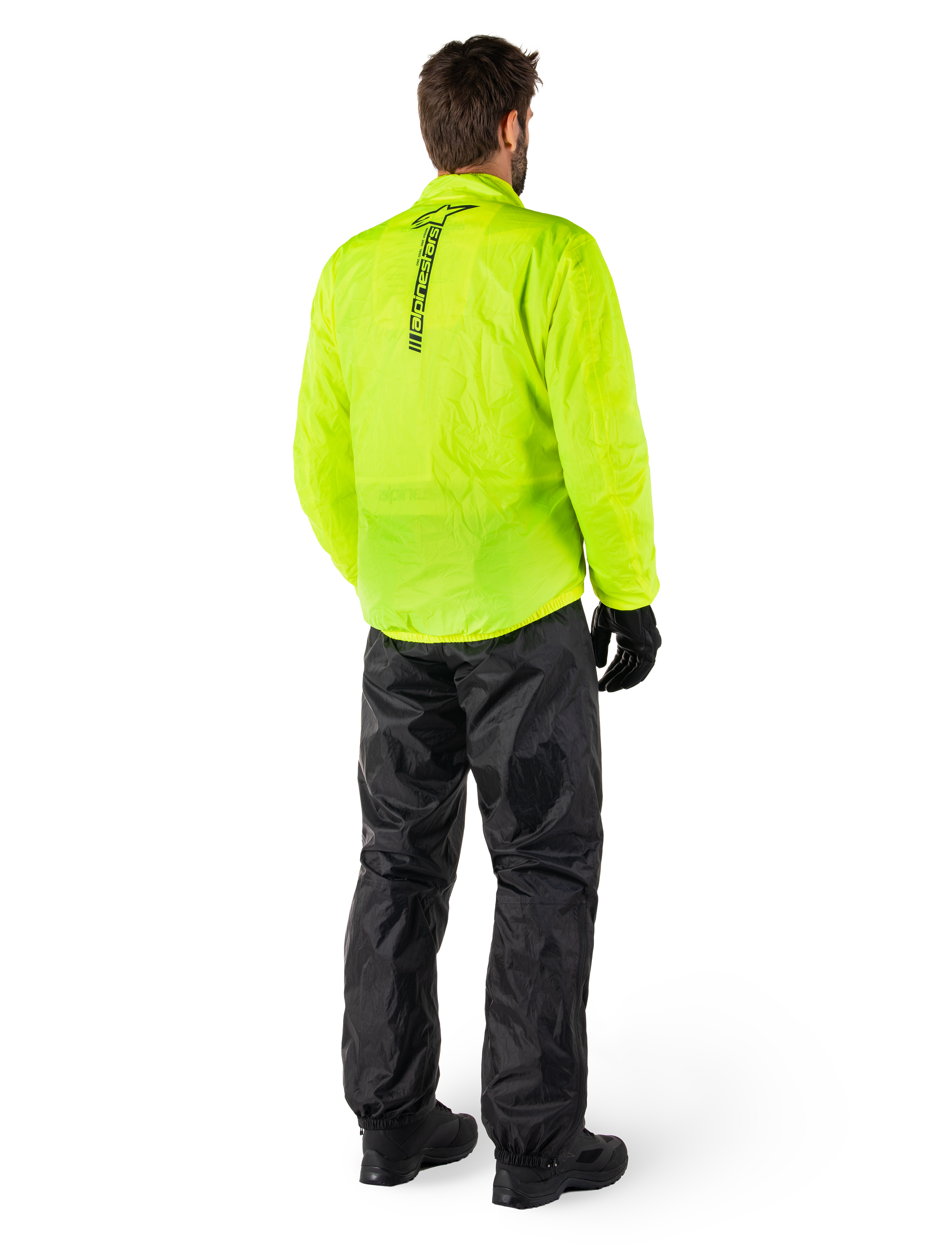 Personne vue de dos portant la veste Alpinestars Hurricane Rain V2 en Jaune Fluo et le pantalon Hurricane Rain V2 en Noir, logo vertical au dos de la veste, équipement de pluie moto imperméable avec gants et bottes noirs