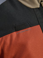 Détail en gros-plan de la veste Alpinestars Andes V4 Drystar® Walnut Rust Black, mettant en avant la boucle pour tuyau d'hydratation intégrée sur la poitrine et la construction en textile ripstop durable.