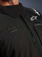 Alpinestars Andes V4 Drystar® Jacke, Schwarz, Nahaufnahme der Brustpartie mit Trinkschlauch-Schlaufe, wasserdichtem VISLON®-Frontreißverschluss und Alpinestars-Logo auf strapazierfähigem Textilmaterial