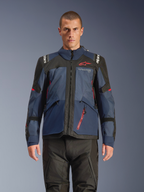 Alpinestars Andes V4 Drystar® Jacke, Adventure-Motorradjacke, Night Navy und Mood Indigo mit schwarzen Einsätzen, getragen von Model mit schwarzer Fahrhose, rotes Alpinestars-Logo auf der Brust und rotes Reißverschluss-Detail, strapazierfähige Textilkonstruktion für Allwetter-Touren.