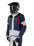 Veste Alpinestars ST-1 Waterproof, veste de moto d'aventure touring en bleu foncé, noir et rouge vif, portée avec un casque noir et des gants gris, dotée d'un design moderne avec des poches fonctionnelles et le logo Alpinestars.