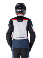 Veste imperméable Alpinestars ST-1, bleu foncé, noir et rouge vif, vue arrière montrant le panneau dorsal gris clair et le logo, veste de moto adventure touring portée avec un casque et des gants noirs, design épuré pour rouler par tous les temps