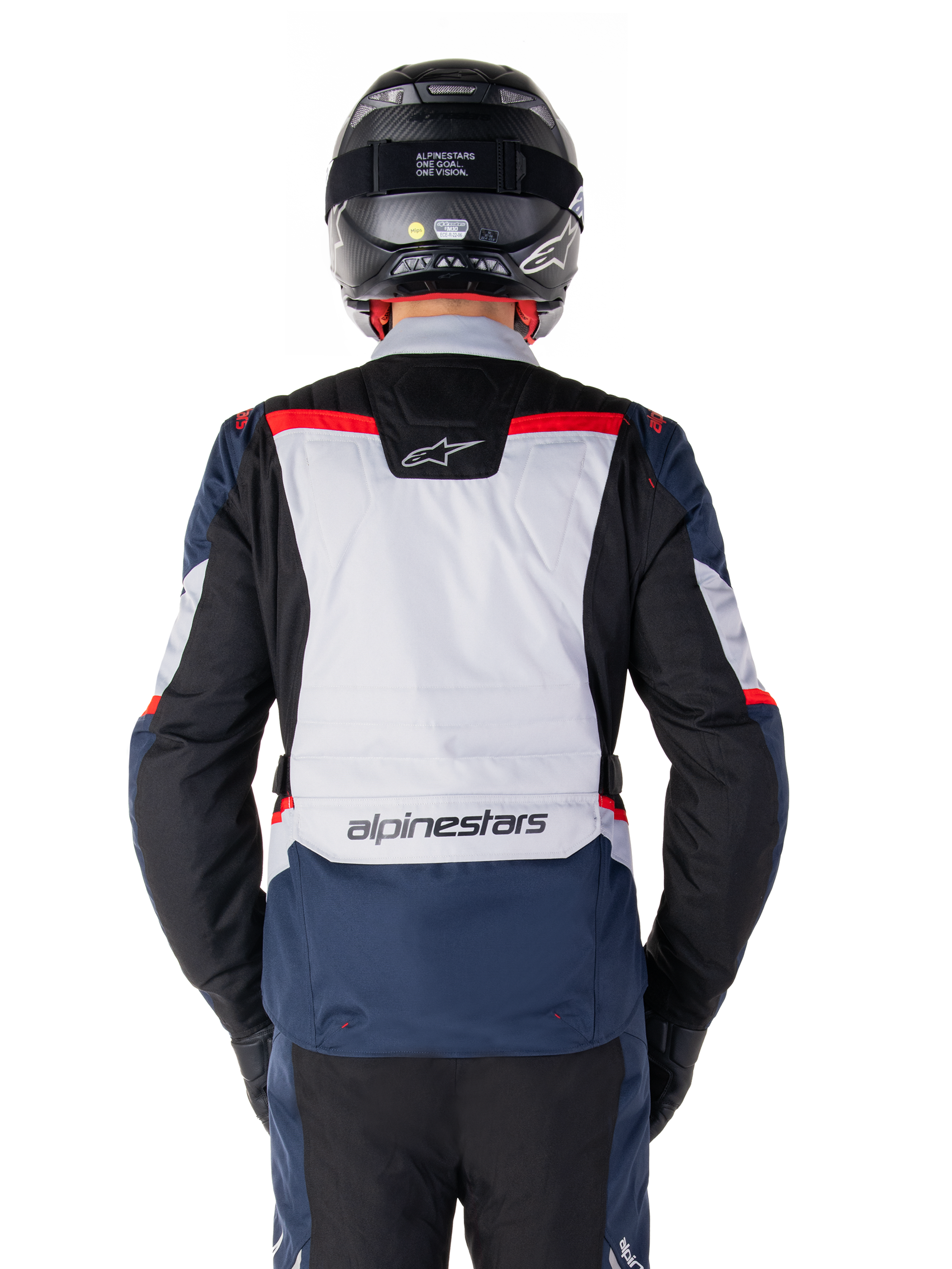 Veste imperméable Alpinestars ST-1, bleu foncé, noir et rouge vif, vue arrière montrant le panneau dorsal gris clair et le logo, veste de moto adventure touring portée avec un casque et des gants noirs, design épuré pour rouler par tous les temps