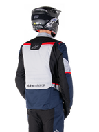 Veste imperméable Alpinestars ST-1, bleu foncé, noir et rouge vif, vue arrière d'un pilote portant un casque d'aventure noir, avec des panneaux gris clair et le marquage Alpinestars, équipement de moto adventure touring