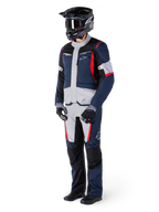 Veste Alpinestars ST-1 Waterproof, veste de tourisme d'aventure, bleu foncé, noir et rouge vif, portée par un motard avec pantalon assorti, casque d'aventure noir, gants et bottes, avec empiècements gris et touches de rouge, design épuré inspiré de l'aventure avec logos Alpinestars