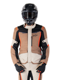 Alpinestars ST-1 Wasserdichte Jacke, Dark Khaki Sand Black Red Fluo, getragen von einem Fahrer mit schwarzem Helm und Handschuhen, Adventure-Touring-Ausrüstung mit beigen und braunen Paneelen und leuchtend roten Fluo-Akzenten, Vorderansicht auf weißem Hintergrund.