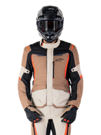 Alpinestars ST-1 Wasserdichte Jacke, Dark Khaki Sand Black Red Fluo, getragen von einem Fahrer mit schwarzem Helm und Handschuhen, Adventure-Touring-Ausrüstung mit beigen und braunen Paneelen und leuchtend roten Fluo-Akzenten, Vorderansicht auf weißem Hintergrund.