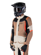 Alpinestars ST-1 Wasserdichte Jacke, Adventure-Touring-Jacke, Dark Khaki Sand Black und Red Fluo, getragen von einem Fahrer mit einem schwarzen Motocross-Helm und einer Brille, mit einem Multi-Panel-Design mit Cargo-Taschen und Alpinestars-Branding auf der Brust
