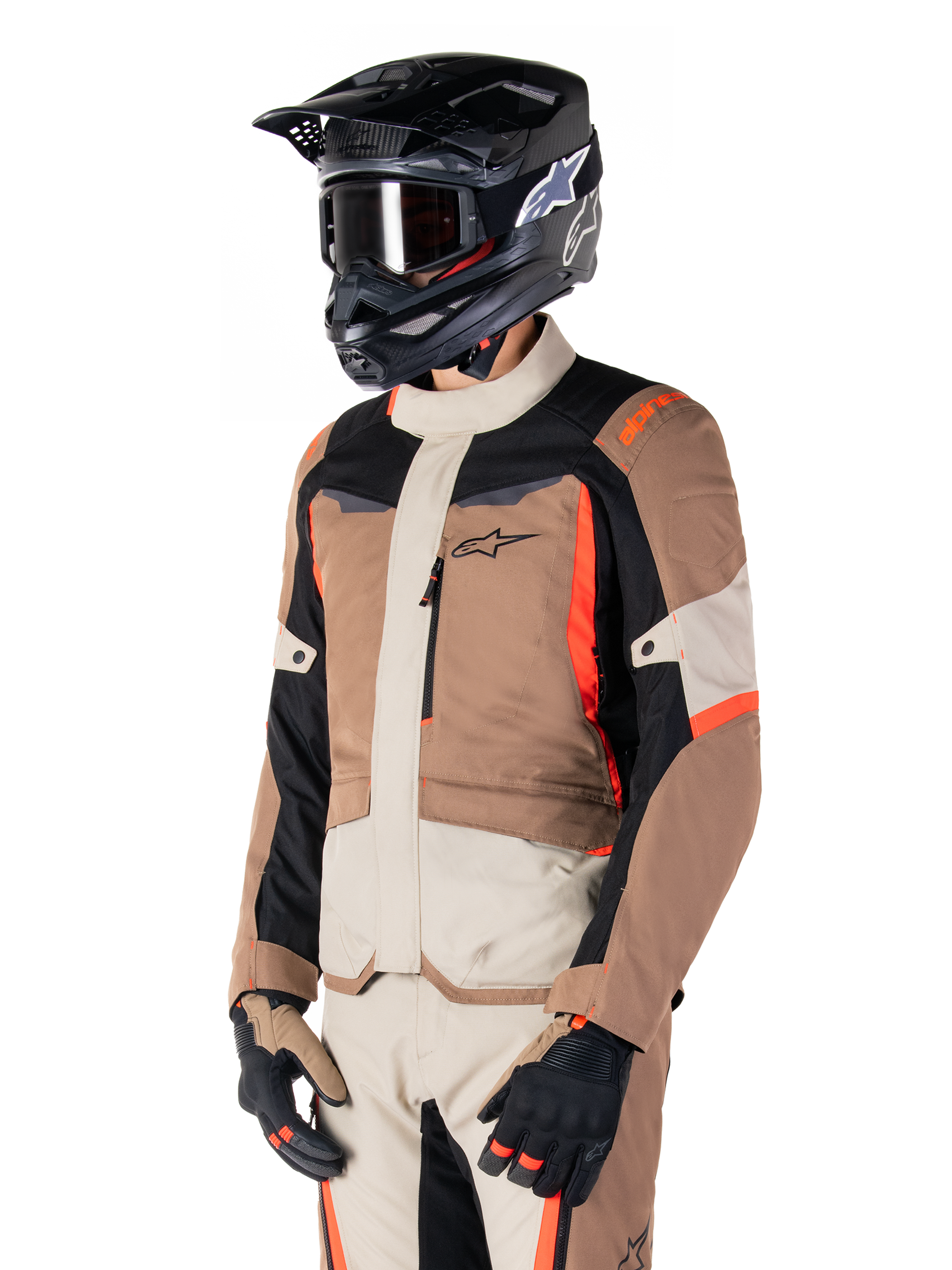 Alpinestars ST-1 Wasserdichte Jacke, Adventure-Touring-Jacke, Dark Khaki Sand Black und Red Fluo, getragen von einem Fahrer mit einem schwarzen Motocross-Helm und einer Brille, mit einem Multi-Panel-Design mit Cargo-Taschen und Alpinestars-Branding auf der Brust