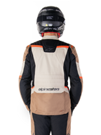 Alpinestars ST-1 Waterproof Jacket, Dark Khaki Sand Black Red Fluo, Rückansicht, Adventure-Touring-Motorradjacke mit einem großen sandfarbenen Rückeneinsatz, schwarzen Ärmeln und leuchtend roten Akzenten, gezeigt an einem Fahrer mit schwarzem Helm.