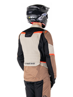 Alpinestars ST-1 Waterproof Jacke, Adventure-Touring-Jacke, Dark Khaki Sand Black Red Fluo, Rückansicht mit Textilpaneelen im Color-Block-Design, fluoreszierend roten Akzenten und Alpinestars-Branding am unteren Rücken, getragen von einem Fahrer mit schwarzem Helm.