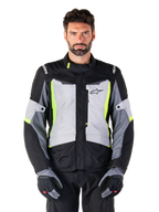 Alpinestars ST-1 Waterproof Jacket, adventure touring motorcycle jacket, Ice Gray Black and Yellow Fluo, worn by a man with matching gloves and black pants, featuring neon yellow accents on the chest and collar, Alpinestars logo on the chest