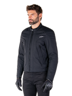 Alpinestars Clayton WR Jas, zwart, urban textiele motorjas met gewatteerde details op de schouders en onderarmen, slim-fit ontwerp, matte afwerking, gedragen door een motorrijder met zwarte handschoenen