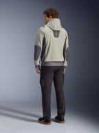 Male model viewed from the back wearing the Alpinestars Moblast Waterproof Jacket in Iron Gray Dark Sage, hooded urban motorcycle jacket with dark gray side panels and reinforced elbow patches, paired with dark riding pants and black sneakers, modern minimalist aesthetic for urban commuting.