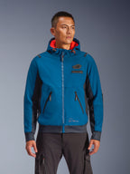 Alpinestars Moblast Waterproof Jacket gedragen door model, blauw en donkerblauw, urban motorjas, ontwerp met capuchon en rode binnenvoering, zwarte ritsen en patchdetail op de borst, op streetwear geïnspireerde motorkleding