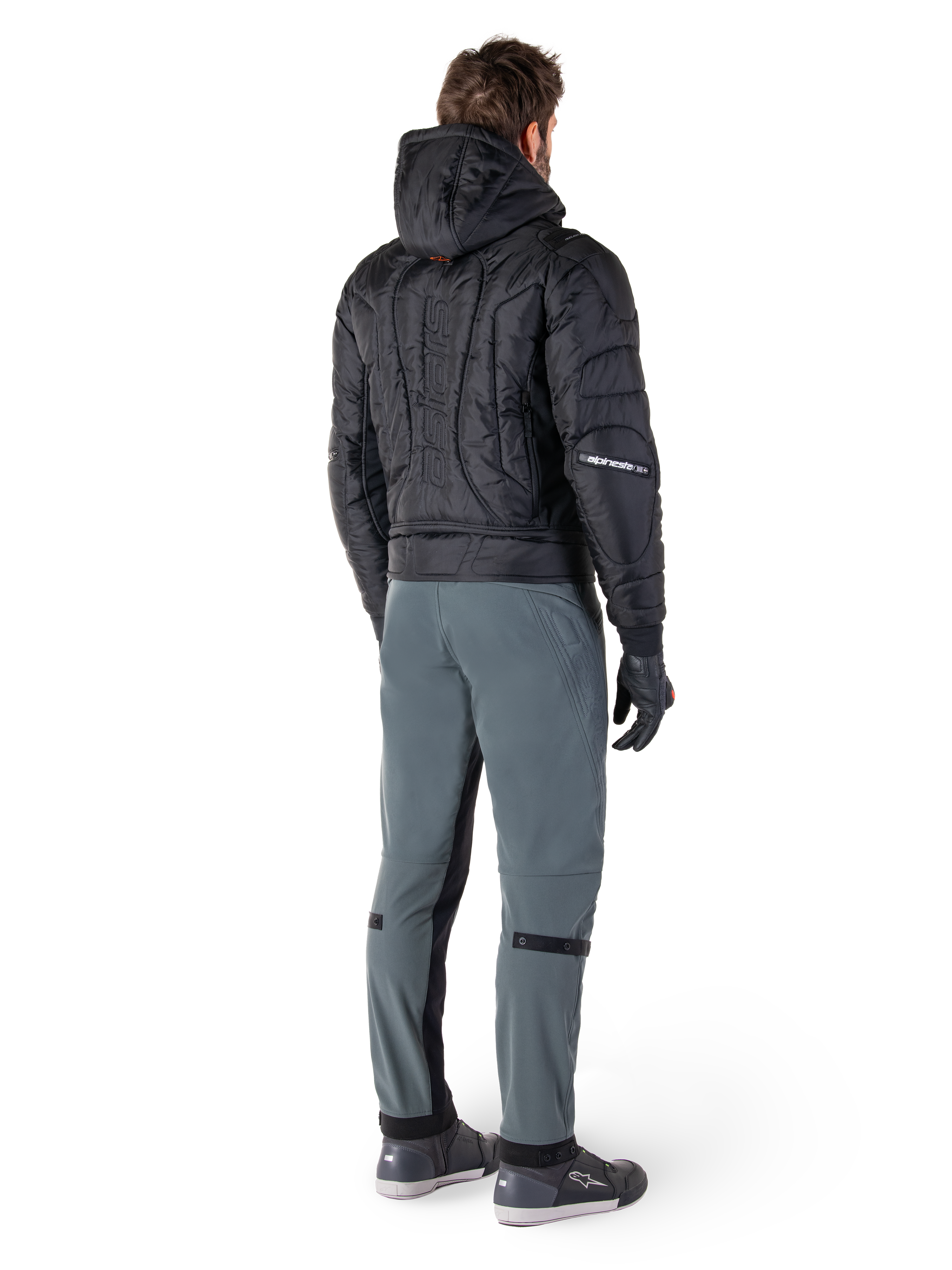 Alpinestars Mohobbs Waterproof Jacket, zwart, achteraanzicht van gewatteerd bomberjack met verticaal woordmerk in reliëf op de rug, gestyled met grijze motorbroek en zwarte handschoenen, op urban streetwear geïnspireerde motorkleding