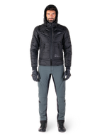 Alpinestars Mohobbs Waterproof Jas in zwart, mannelijk model draagt een gewatteerd bomberjack met capuchon, gecombineerd met een grijze motorbroek, zwarte handschoenen en zwarte laarzen, urban contemporary motoruitrusting