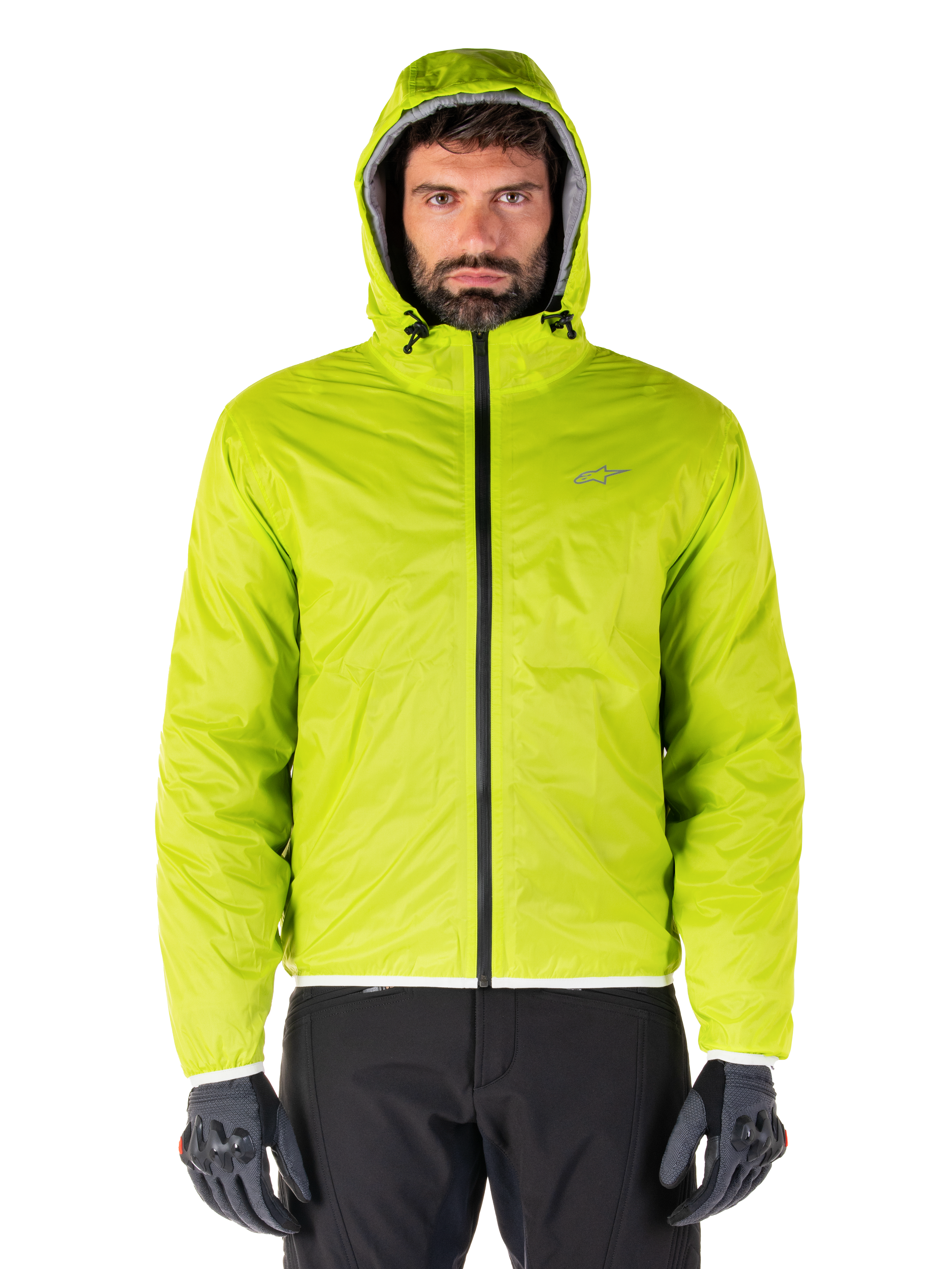 Alpinestars Mohobbs Wasserdichte Jacke, verstaubarer Regenschutz in Lime Punch, hell neongrüne Kapuzenjacke kombiniert mit schwarzer Motorradhose und grauen Motorradhandschuhen, urbaner Moto-Streetwear-Stil.