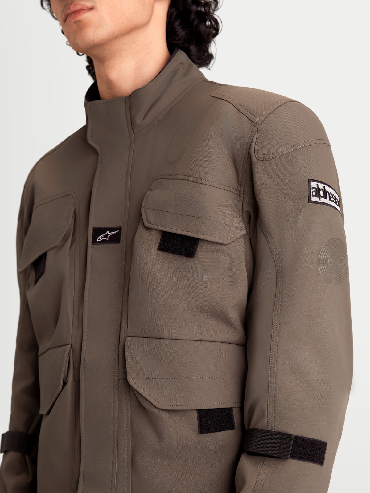 Alpinestars Altan Drystar Jacket, men's urban contemporary motorcycle textile jacket in walnut and black, close-up view showing field-jacket storage cargo pockets, matte polyfabric construction, and shoulder armor detail worn by a model.