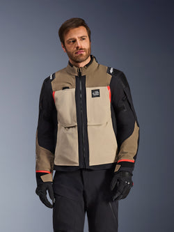 Alpinestars Andes Pro Drystar® XF Jas, Walnut Aluminum, adventure motorjas met beige en zwarte panelen en rode accenten, gedragen met een zwarte motorbroek en handschoenen, technische waterdichte touringuitrusting