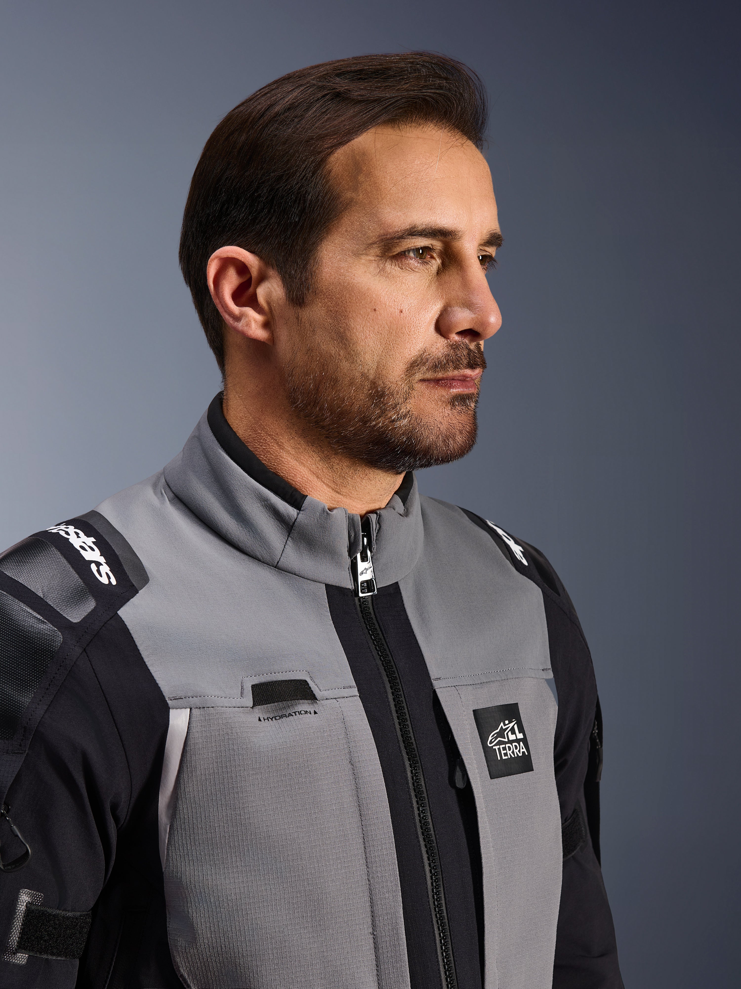 Alpinestars Andes Pro Drystar® XF Jacke, Motorrad-Abenteuerjacke, Dunkelgrau und Schwarz, Nahaufnahme von Vorderseite und Kragen, mit Terra-Branding und Details zur Trinkschlauchführung, getragen von einem Mann in einer Studio-Umgebung