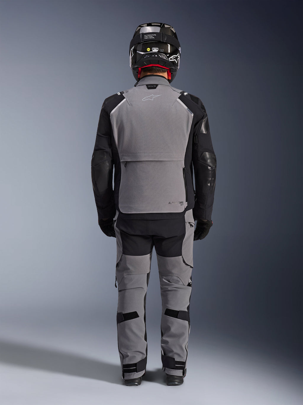 Alpinestars Andes Pro Drystar® XF Jacke, Rückansicht, dunkelgraue und schwarze Adventure-Touring-Ausrüstung, kombiniert mit passender grau-schwarzer Hose, schwarzem Carbonhelm und schwarzen Handschuhen, mit technischen Einsätzen und reflektierendem Branding
