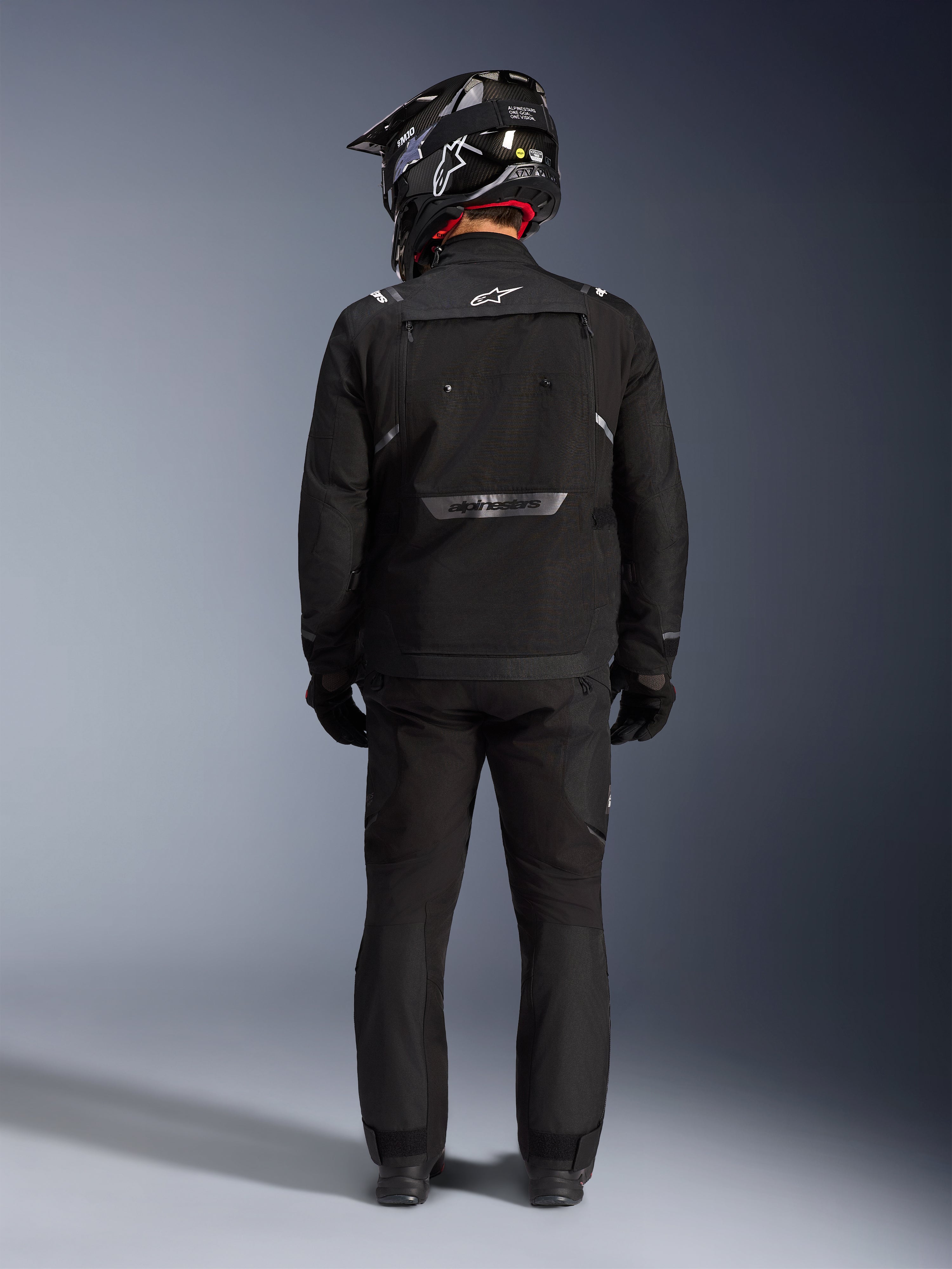 Alpinestars Cusco Drystar Jacket, Motorcycle Adventure Jacket, Black, back view worn with matching pants and a black and white helmet, featuring reflective Alpinestars branding and large ventilation panels, durable textile construction for road adventure touring