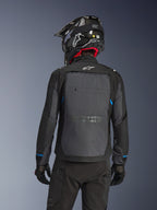 Pilote vu de dos portant la veste Alpinestars Cusco Drystar® en Noir et Gris Foncé, dotée d'un grand panneau de ventilation arrière gris et d'un logo blanc, accompagnée d'un casque tout-terrain noir et d'un équipement de moto noir pour l'adventure touring.