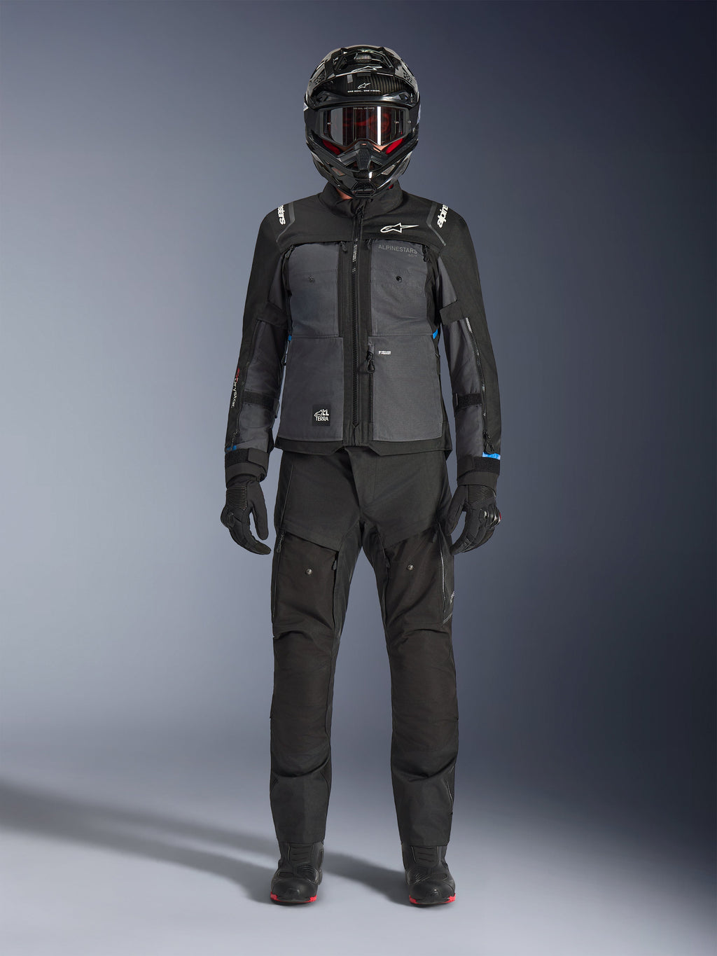 Veste Alpinestars Cusco Drystar®, veste d'aventure touring noir et gris foncé, portée avec un pantalon noir, des gants et un casque intégral assortis, vue de face en pied, vêtement de protection pour moto