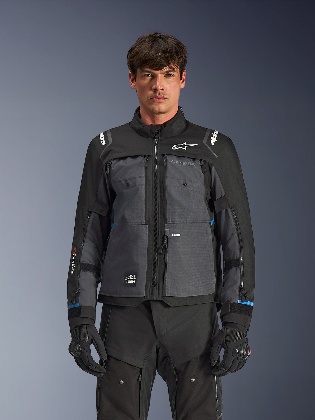 Veste Alpinestars Cusco Drystar®, veste de moto touring, noir et gris foncé, vue de face sur modèle, avec logos Alpinestars sur la poitrine et les épaules, marquage Drystar® sur la manche, design technique multi-poches avec zips de ventilation, associée à un équipement de moto noir
