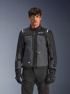 Veste Alpinestars Cusco Drystar®, veste de moto touring, noir et gris foncé, vue de face sur modèle, avec logos Alpinestars sur la poitrine et les épaules, marquage Drystar® sur la manche, design technique multi-poches avec zips de ventilation, associée à un équipement de moto noir