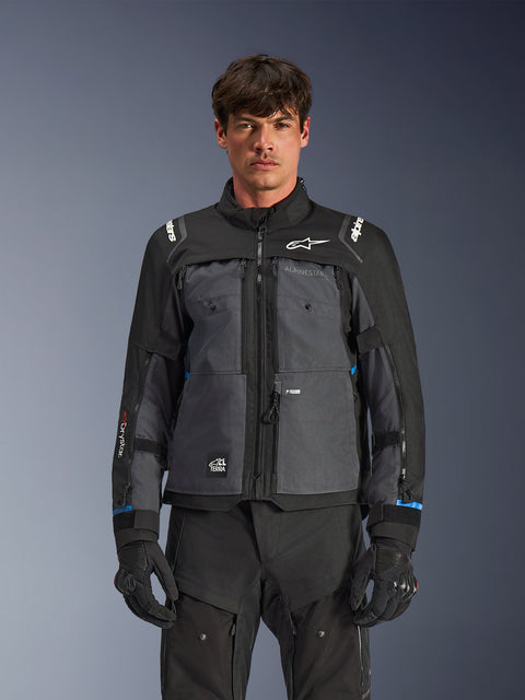 Veste Alpinestars Cusco Drystar®, veste de moto touring, noir et gris foncé, vue de face sur modèle, avec logos Alpinestars sur la poitrine et les épaules, marquage Drystar® sur la manche, design technique multi-poches avec zips de ventilation, associée à un équipement de moto noir