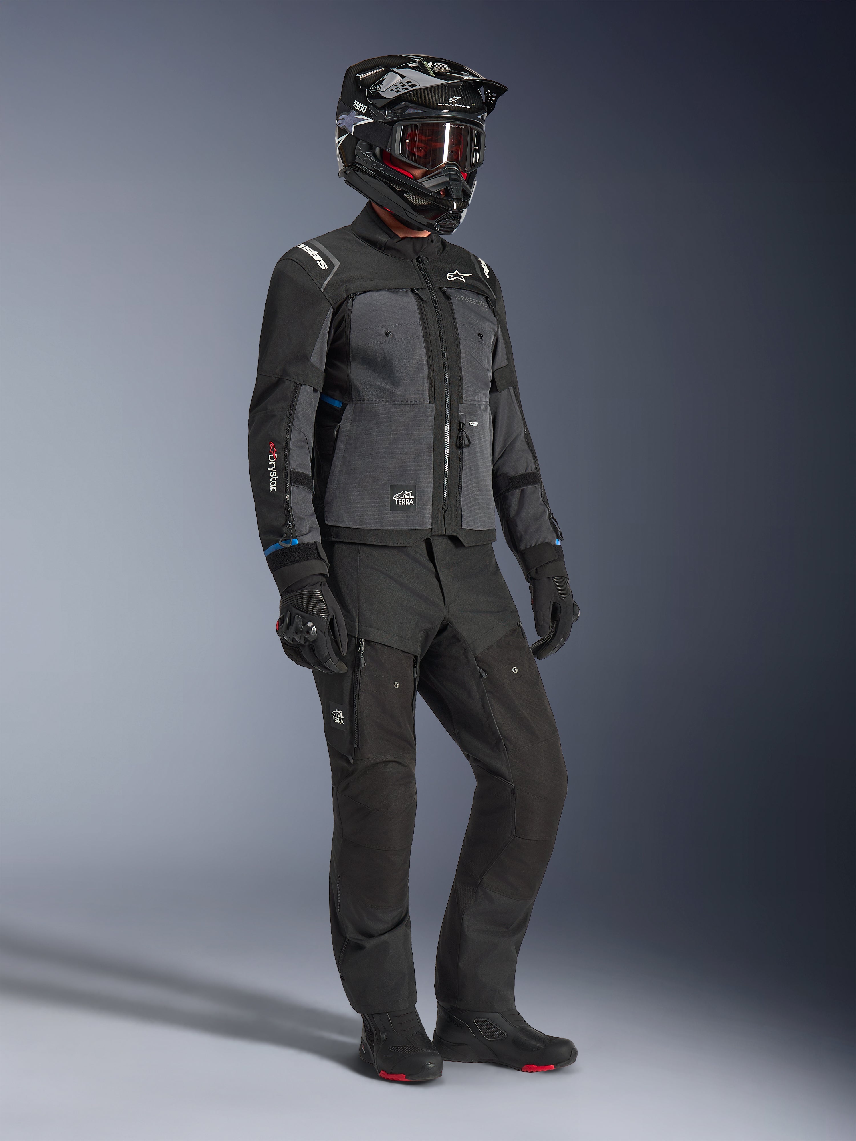 Mannequin portant la veste Alpinestars Cusco Drystar® en Noir et Gris foncé, associée à une tenue de moto complète incluant un casque noir, un pantalon technique assorti, des gants et des bottes, avec une construction en ripstop et softshell pour la route et l'adventure touring