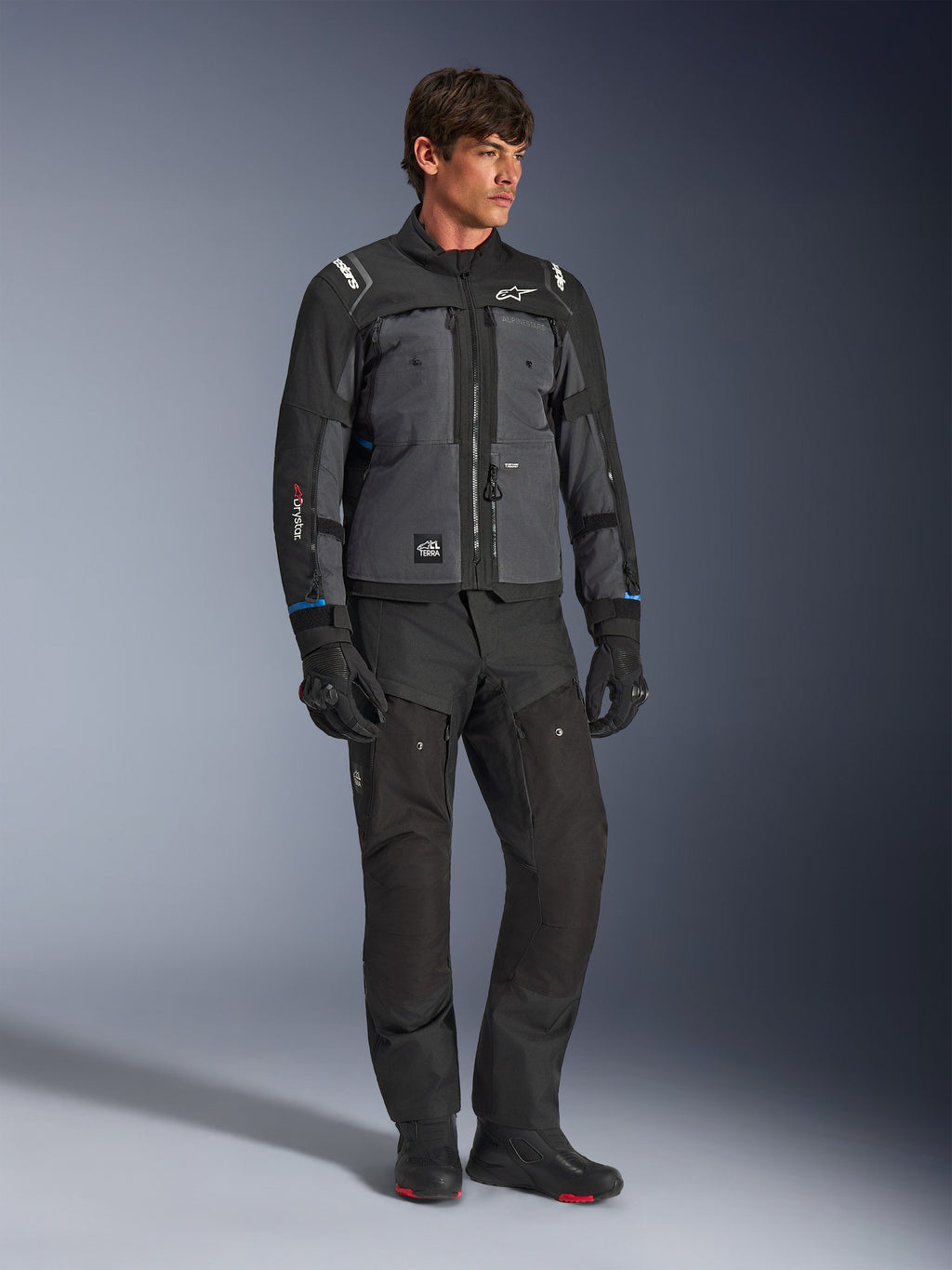 Veste Alpinestars Cusco Drystar® en noir et gris foncé, veste technique de touring moto avec empiècements multi-tons, portée avec un pantalon et des gants de moto noirs assortis, conçue pour la route et l'adventure touring.