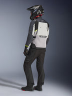 Veste Alpinestars Cusco Drystar®, coloris gris glacé, gris moyen et gris foncé, vue arrière portée par un pilote, accents jaune fluo, large panneau de ventilation au dos avec logo, construction textile durable, tenue de touring complète avec pantalon noir et casque d'aventure.