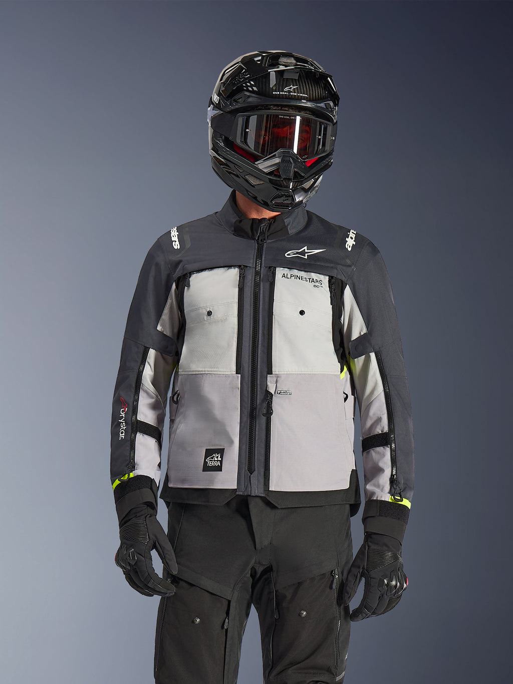 Veste Alpinestars Cusco Drystar®, veste d'aventure touring, coloris Ice Gray Mid Gray et Deep Gray, dotée de panneaux gris multi-tons, de ventilations zippées sur la poitrine et du marquage Alpinestars, portée par un pilote avec un casque et un masque noirs.