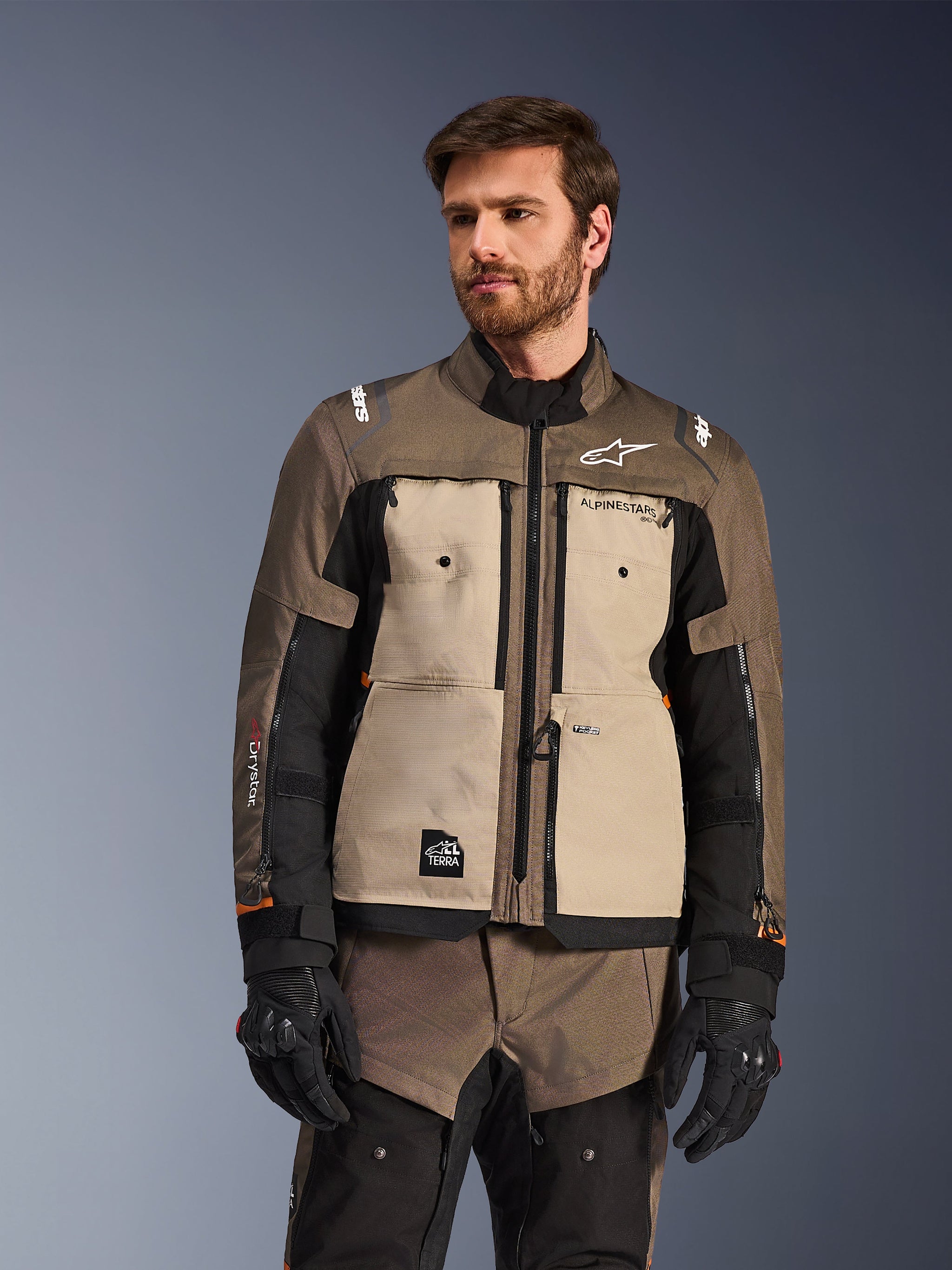 Alpinestars Cusco Drystar® Jacket, Adventure Motorcycle Jacket, Walnut Aluminum Black, worn by a model with black gloves, featuring tan chest panels and black sleeves with Alpinestars branding and All Terra patch, protective all-weather touring gear