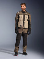 Alpinestars Cusco Drystar® Jacke in Walnut Aluminum Black, getragen von einem männlichen Fahrer mit passender Adventure-Tourenhose, schwarzen Handschuhen und Stiefeln, mit beigen Brustpaneelen, schwarzen Ärmeln mit dezenten orangefarbenen Akzenten und funktionellen Belüftungsreißverschlüssen für Motorrad-Straßenfahrten.