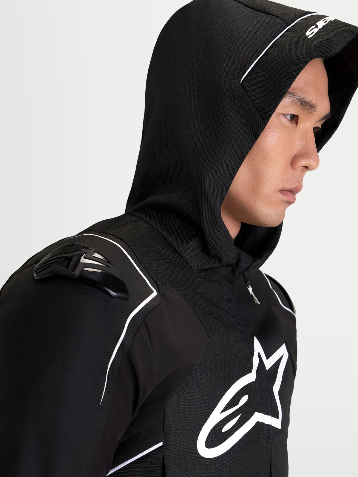 Alpinestars Zaca V2 Waterproof Jacket, men's motorcycle sport jacket in black and white, featuring an integrated hood, DFS shoulder armor, and a prominent Alpinestars chest logo, on-model profile view