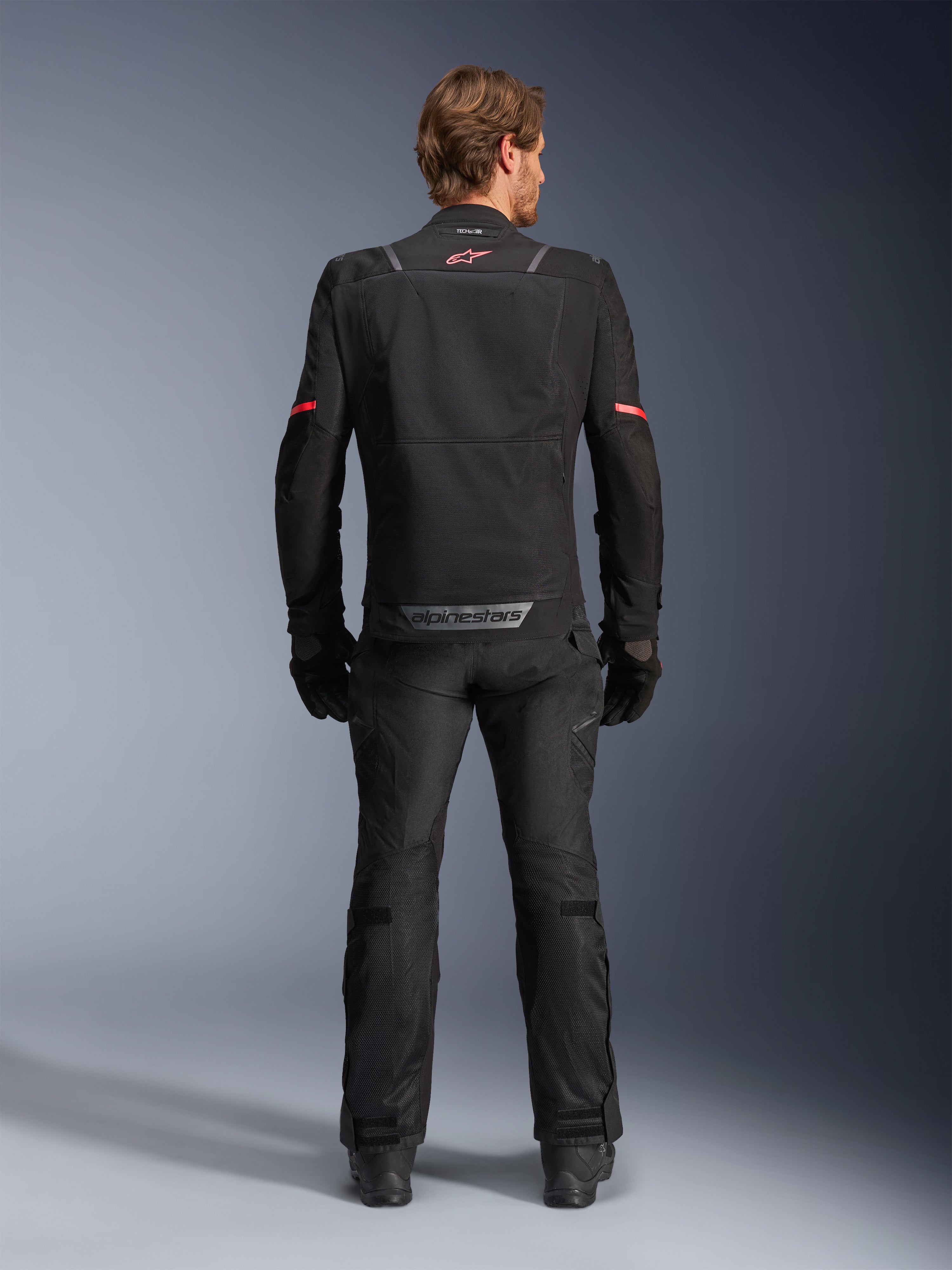 Alpinestars ST-2 Air Jacket, Black, back view of a rider wearing the motorcycle jacket and matching black pants, featuring mesh ventilation panels, red logo on the upper back, and grey Alpinestars branding on the lower back hem