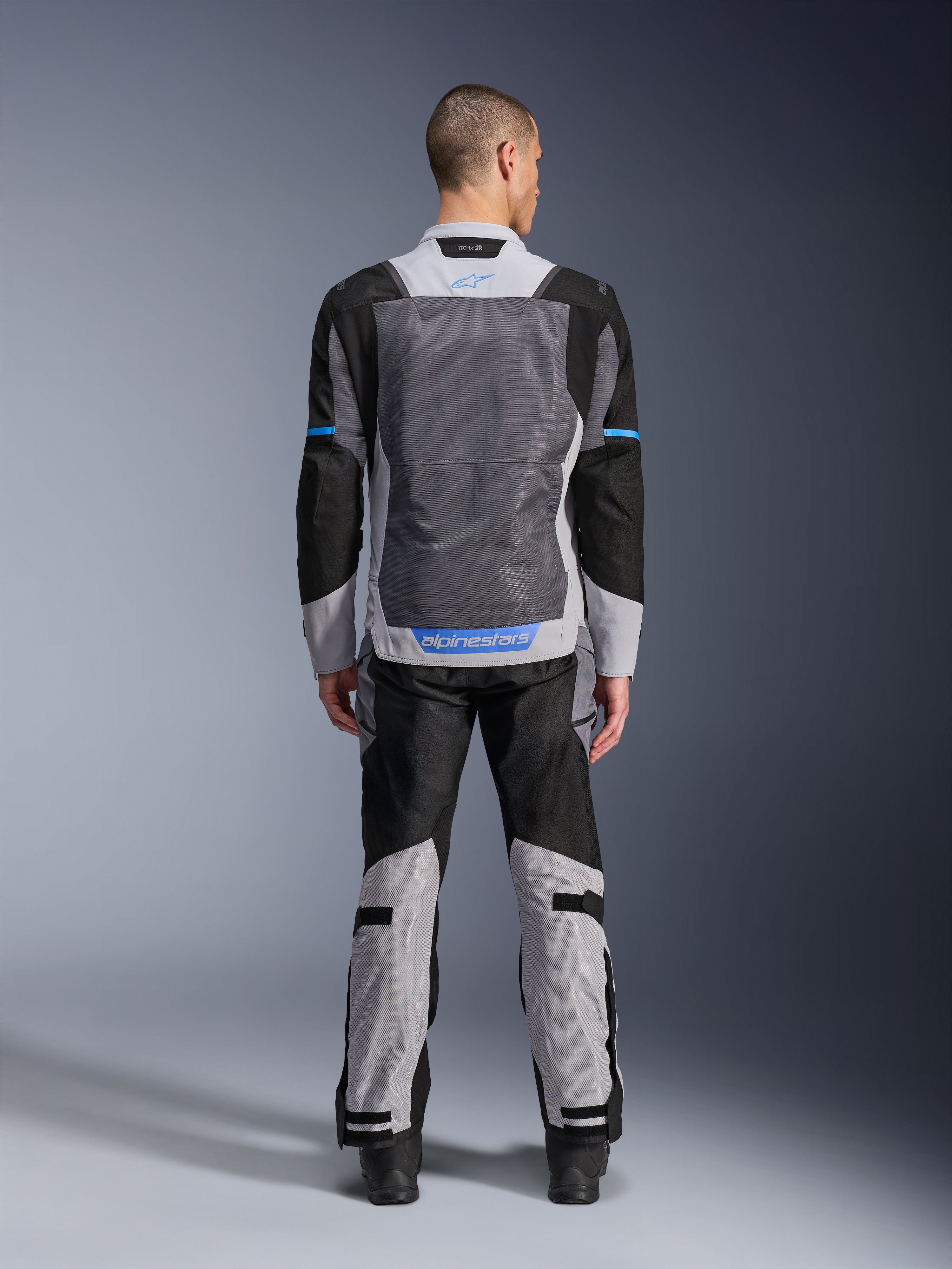 Alpinestars ST-2 Air Jacke, Ice Gray Dark Gray Black, Rückansicht am Modell, mit großen Mesh-Belüftungseinsätzen, blauen Akzenten und Alpinestars-Logo, kombiniert mit passender Motorradhose für Adventure-Touren.
