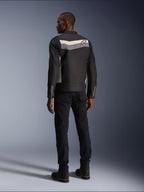 Modèle masculin de dos portant la veste Alpinestars T-Dyno WR en Noir Gris Foncé Écru, veste de moto en textile avec une bande horizontale et le logo étoile au dos, associée à un pantalon de conduite et des bottes noirs, esthétique d'équipement de moto urbain.