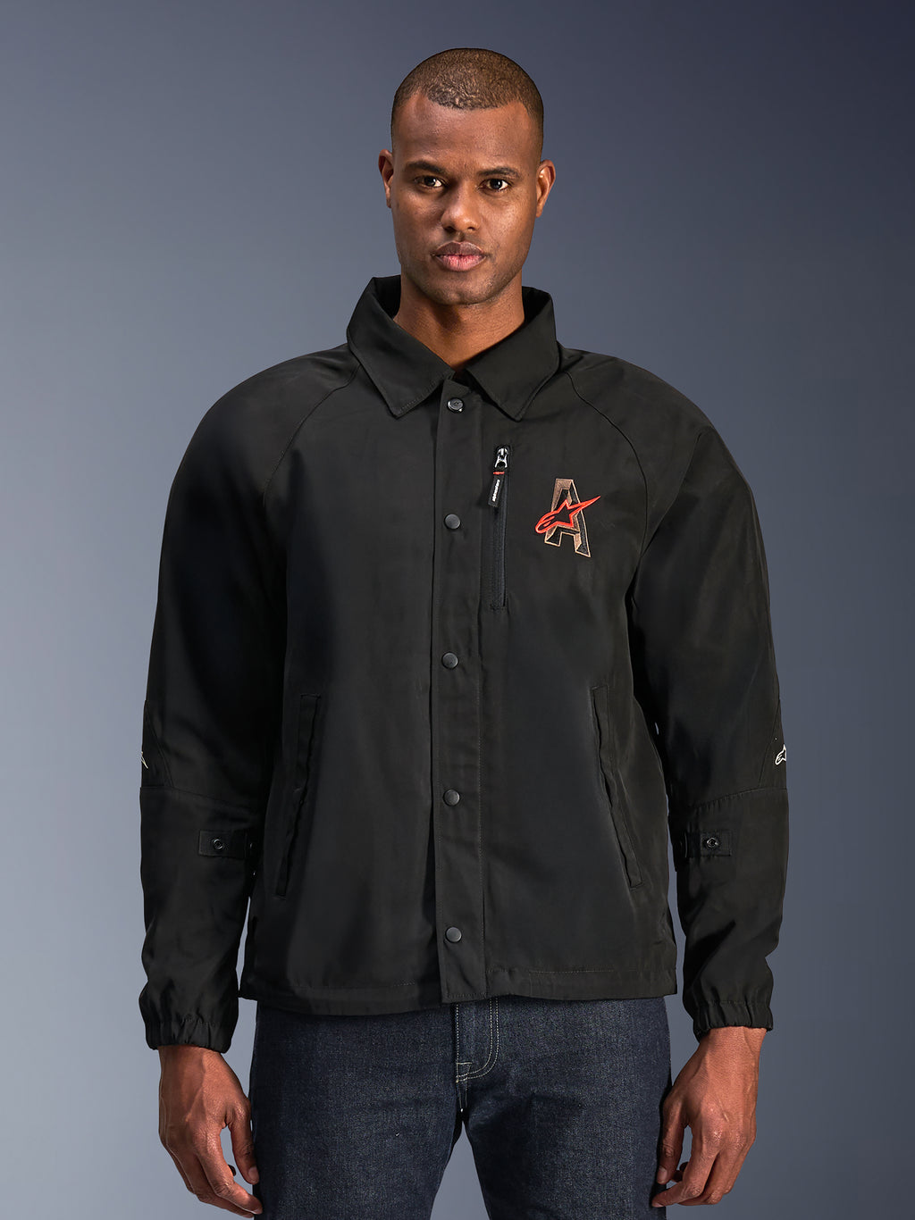 Alpinestars Revved WR Jacket, zwarte motorjas met een overhemdkraag en drukknoopsluiting aan de voorzijde, rood geborduurd 'A'-logo op de borst, verticale borstzak met rits, elastische manchetten, urban coaches jacket ontwerp
