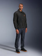 Alpinestars Revved WR Jacket in het zwart, urban motorjas in coaches-stijl gedragen door een model met donkerblauwe jeans en zwarte sneakers, voorzien van een drukknoopsluiting aan de voorzijde en een geborduurd logo, minimalistisch en sportief ontwerp voor rijden op de weg.
